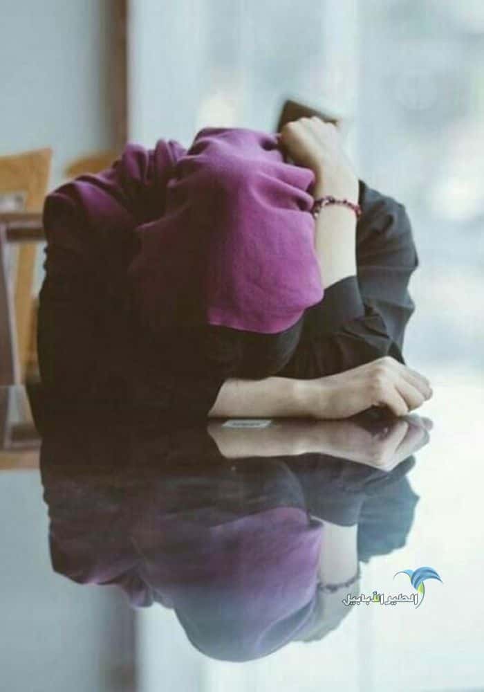 صورة فتاة محجبة تجلس على طاولة زجاجية حزينة وتبكي